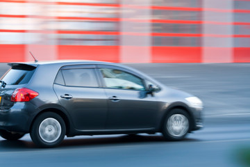 Obraz na płótnie Canvas Gray car moving fast along the road on blurred stripped red background