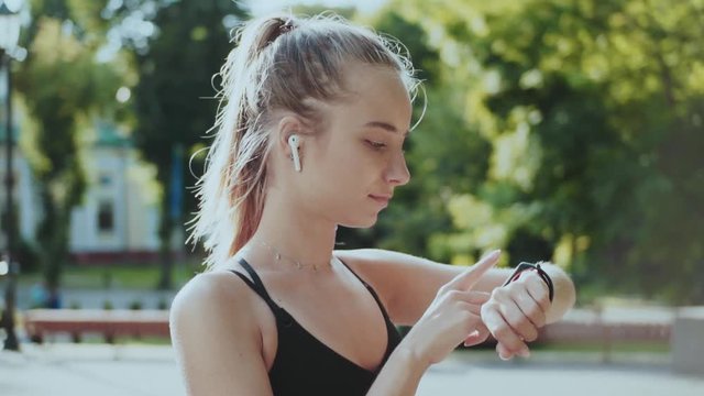 Close up young fitness woman look at smart watch and camera at sunlight outdoors athlete workout equipment app technology active device slow motion