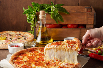 Female hand hold slice of hot pizza with melting cheese and chorizo on rustic wooden table with...