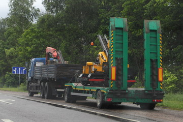 Flatbed truck with green low-frame two-axle trailer trawl a special vehicle on asphalt highway road in the summer day, rear-side view – Logistics, transportation, trucking industry