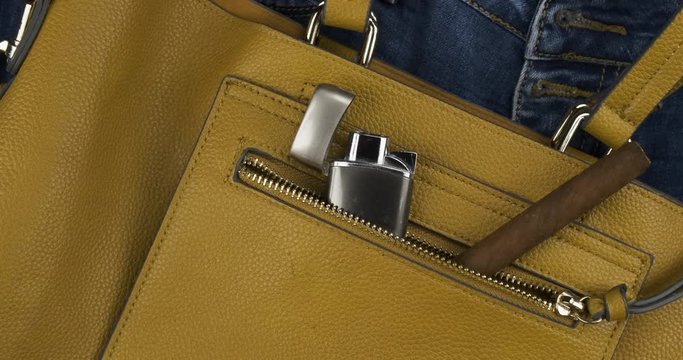 Rotation of a cigar and a lighter protruding from a pocket of a female bag. Bad habits concept. Top view.