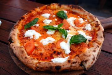 Closeup of Pizza Margherita on wodden table. Typical italian Homemade Pizza Margarita with Tomatoes, Basil and Mozzarella Cheese.
