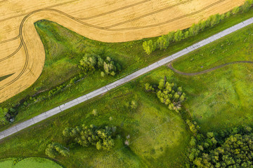 Aerial shot. Asphalt road in green vegetation near a wheat field. In a rural area
