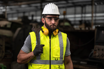 Portrait of technician man or industrial worker with hardhat or helmet, eye protection glasses and vest working electronic machinery on laptop and mechanical  in Factory of manufacturing place