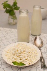 Homemade cottage cheese with a mint leaf in a white ceramic plate and two glass bottles with milk.