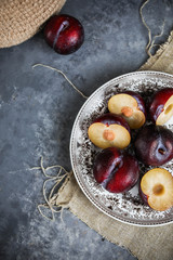 Red plums on a vintage plate on a gray background. Pieces of fruit. View from above.