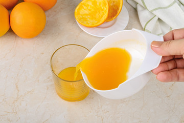 Caucasian woman hands pouring freshly squeezed orange juice from manual citrus juicer into a glass on a kitchen table. Vegetarian, raw food diet and healthy eating.
