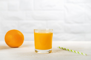Glass of freshly squeezed orange juice, one whole orange and paper drinking straw on a white wooden table. Vegetarian, raw food diet and healthy eating.