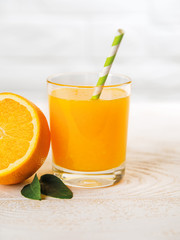 Glass of freshly squeezed orange juice with a drinking straw and half of orange on a white wooden table. Vegetarian, raw food diet and healthy eating. Close-up.