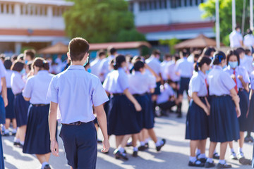 The back view of Asian high school students in white uniforms on the semester start wearing masks during the Coronavirus 2019 (Covid-19) epidemic.