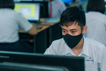 Asian male high school student on the semester start wearing masks in computer classroom during the Coronavirus 2019 (Covid-19) epidemic.