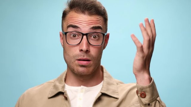 young casual guy fixing his glasses and being took by surprise, scratching his head and then finding a solution on blue background