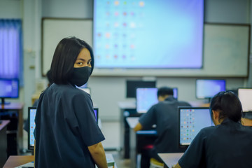 Asian female high school student in blue uniform on the semester start wearing masks in computer classroom during the Coronavirus 2019 (Covid-19) epidemic.