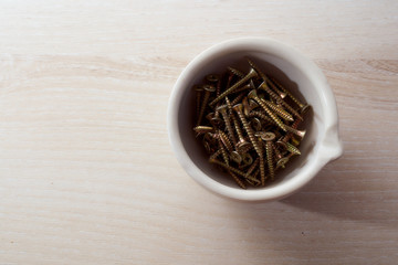 The screws lie in a white cup against a light background. With copy space.Top view.