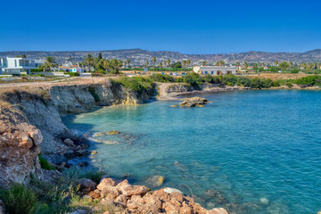 Fototapeta na wymiar A small lagoon with blue sea water on the coast of Paphos, Cyprus. In the distance you can see the hotel with the beach. Waves breaking on coastal cliffs.
