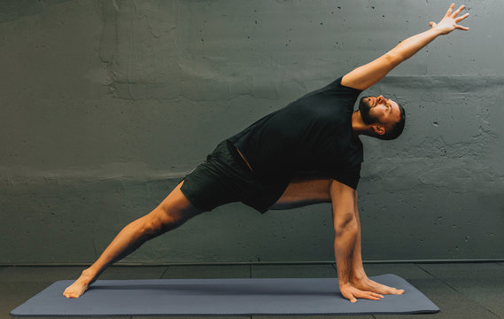 Sporty Young Man Working Out, Doing Handstand Yoga. Studio Shot In Urban Fitness Gym With Grey Background For Copy Space.