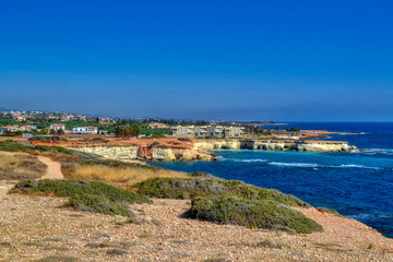 Fototapeta na wymiar A small lagoon with blue sea water on the coast of Paphos, Cyprus. In the distance you can see the hotel with the beach. Waves breaking on coastal cliffs.