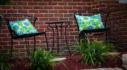 Two metal garden chairs with colorful pillows in from of brick wall
