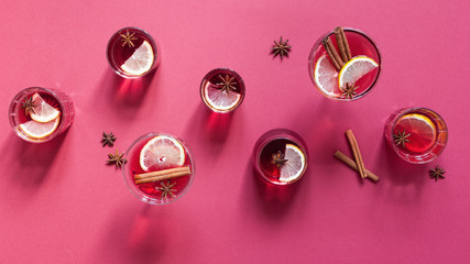 Glasses of mulled wine, orange slices, cinnamon and anise stars on red background with shadows top view.