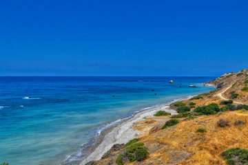 Fototapeta na wymiar View of the Aphrodite's beach from the mountain observation platform on a sunny hot day. The famous beach on the island of Cyprus, near the town of Paphos.