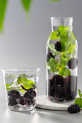 infused water with blackberries and mint in a bottle and a glass. healthy refreshing drink. Gray background. vertical image. copy space.
