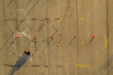 top down wide aerial view of one rider practicing on an advanced motorcycle training slalom course between orange cones with long shadows, tire marks and painted lines