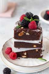 close-up of chocolate brownie cake pieces with hazelnuts, raspberries and blackberries. Ready for eating. Gray background. vertical image