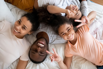 Precious moments. Top portrait of happy black father and biracial mother lying on bed together with two children daughter and son, friendly loving african family of four smiling and looking at camera