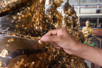 Hand of a woman with gold leaf on a buddha statue