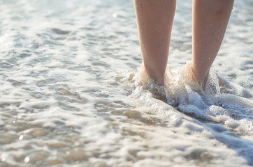 Women's legs are covered by the sea wave. Feet in the water close-up.
