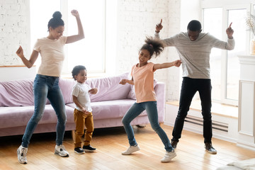 Dancing indoors. Happy black millennial parents and two children daughter and son enjoying dances...