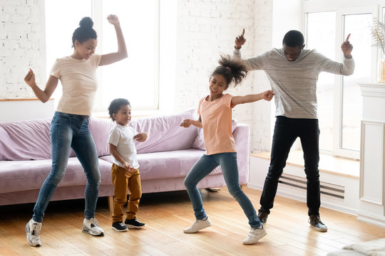 Dancing indoors. Happy black millennial parents and two children daughter and son enjoying dances in living room, active african family dad, mom and kids handle stress of being at home on quarantine