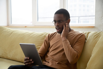 Amazed african american man reading shocking news on tablet screen. Young black guy shocked browsing online at home, stressed with bills and payments use digital touch pad computer
