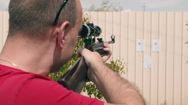 Close up of the face of a man aiming at an impromptu paper target while looking into an optical rifle sight.