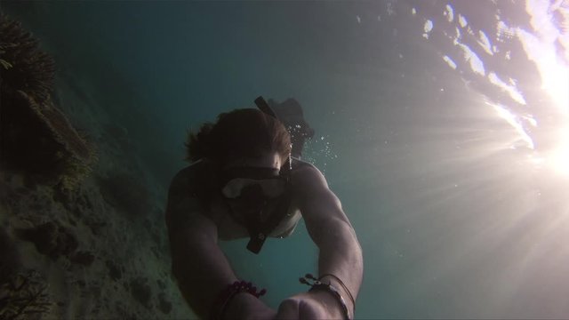 Man rotate underwater while swimming with fins above sandy floor
