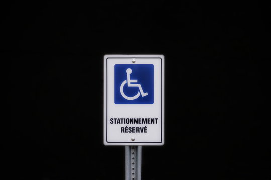 Close up of an handicap  disabled person reserved parking space  sign in french stationnement réservé on a black background
