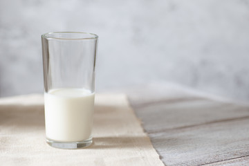 High transparent glass of milk on a wooden table on a gray background in a high key