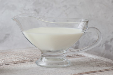 transparent jug of milk on a wooden table on a gray background in a high key
