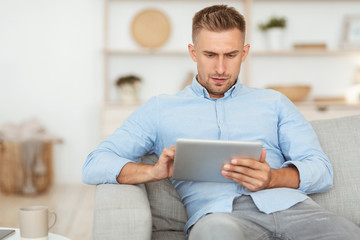 Happy man using digital tablet sitting on sofa