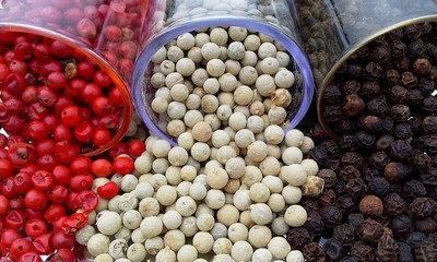 Extreme close up of three kinds of peppercorn white red black from spilled glasses full frame
