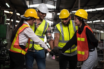 Technicians and Engineer workers  with hardhat or helmet, vest showing hands coordination and raising fist smiling for successful working in workplace of industry Factory/Teamwork co-workers