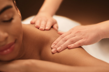 Fototapeta na wymiar Masseuse hands massaging african woman shoulders, relaxing body massage