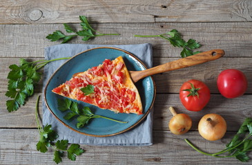 Advertising background with homemade pizza with tomatoes, cheese, sausage.Sprigs of parsley are laid out around the sliced slice of pizza on a plate on a wooden backgroun