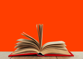 Open book textbook in a red cover on a wooden desk with orange background. Back to school distance home education.Quarantine concept of stay home.
