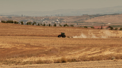 Obraz premium A tractor plowing a field in a farm with yellow grass.