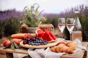 A summer picnic in a lavender field with watermelon, croissants and a bottle of rose wine and two glasses. Beautiful rustic decor.