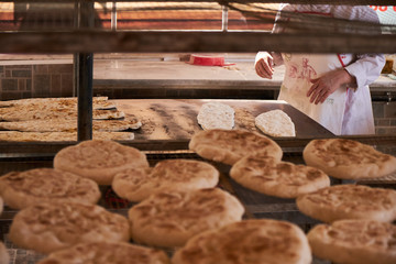 Fluffy flatbreads in bakery shelves, woman cook in the background. 