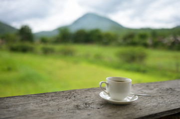 Cup of coffee on a wooden table over mountains landscape and rice field with sunlight. Beauty nature background