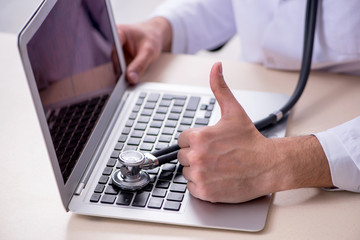 Young male doctor with stethoscope repairing computer