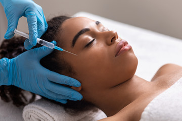 Obraz na płótnie Canvas Young black lady receiving eye zone injection at beauty salon